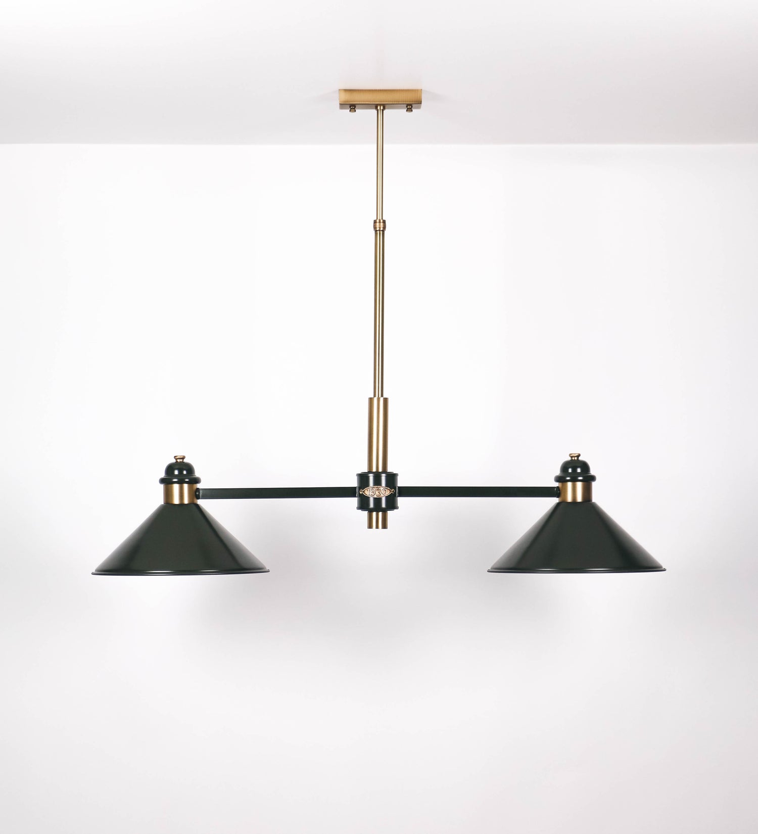 Suspensão de teto moderna e sofisticada. A suspensão é composta por uma base retangular em ouro velho, de onde desce um tubo cilíndrico até a estrutura principal e permite ajustar a altura da suspensão. A estrutura principal é composta por uma barra horizontal verde-azeitona, que sustenta nas extremidades dois chapéus cónicos invertidos no mesmo tom, com interior em ouro velho. No centro da barra horizontal está uma pequena placa oval, em ouro velho, com o ano 1930 inscrito em relevo.