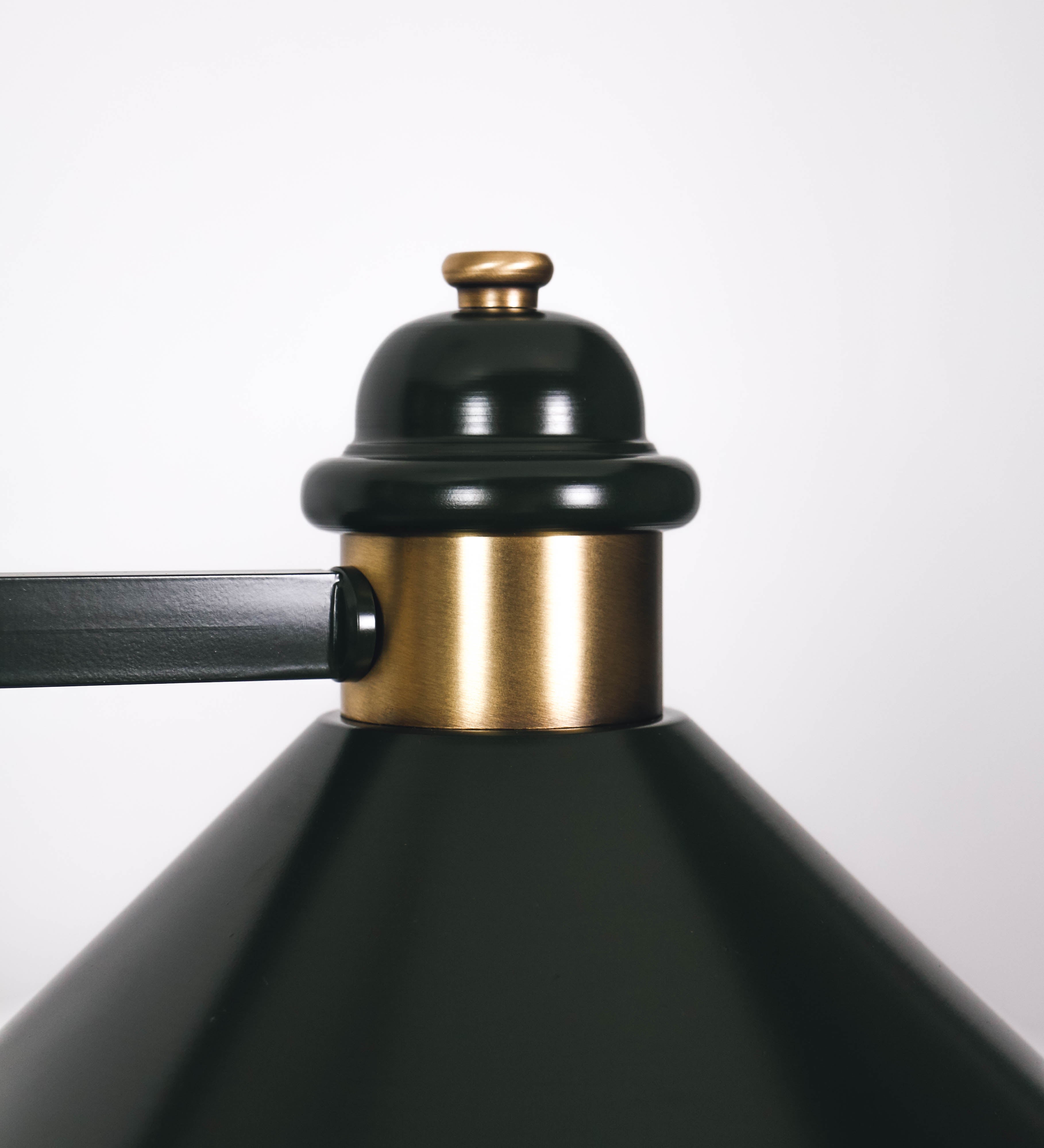 Suspensão de teto moderna e sofisticada. A suspensão é composta por uma base retangular em ouro velho, de onde desce um tubo cilíndrico até a estrutura principal e permite ajustar a altura da suspensão. A estrutura principal é composta por uma barra horizontal verde-azeitona, que sustenta nas extremidades dois chapéus cónicos invertidos no mesmo tom, com interior em ouro velho. No centro da barra horizontal está uma pequena placa oval, em ouro velho, com o ano 1930 inscrito em relevo.