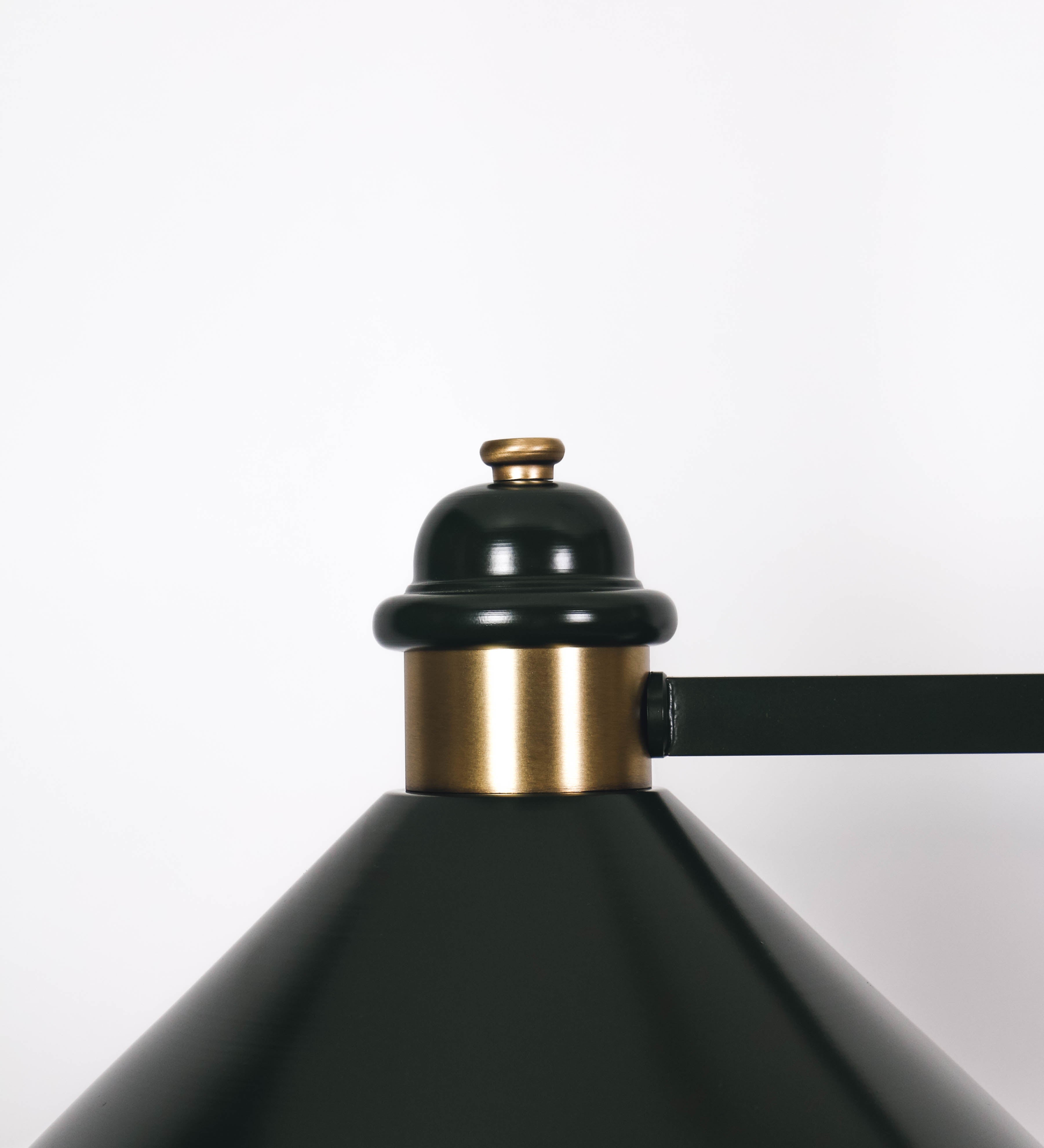 Suspensão de teto moderna e sofisticada. A suspensão é composta por uma base retangular em ouro velho, de onde desce um tubo cilíndrico até a estrutura principal e permite ajustar a altura da suspensão. A estrutura principal é composta por uma barra horizontal verde-azeitona, que sustenta nas extremidades dois chapéus cónicos invertidos no mesmo tom, com interior em ouro velho. No centro da barra horizontal está uma pequena placa oval, em ouro velho, com o ano 1930 inscrito em relevo.
