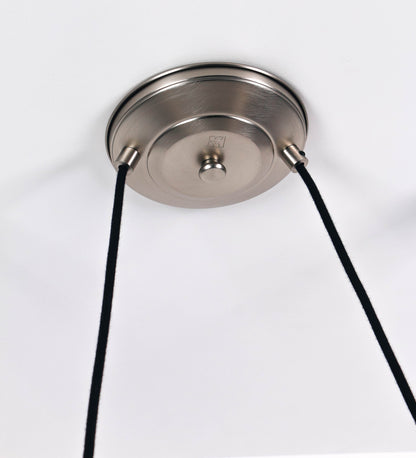 Suspensão de teto dupla em níquel escovado, composta por uma base circular de onde descem dois cabos revestidos têxtil pretos. Cada cabo passa por uma roldana fixa ao teto, e desce até aos chapéus. Entre a base e as roldanas, cada cabo sustenta uma esfera que atua como contrapeso para ajustar a altura do candeeiro. Os dois chapéus são de formato cónico invertido e com uma borda ligeiramente levantada. No topo de cada chapéu há um suporte que conecta os chapéus aos cabos.