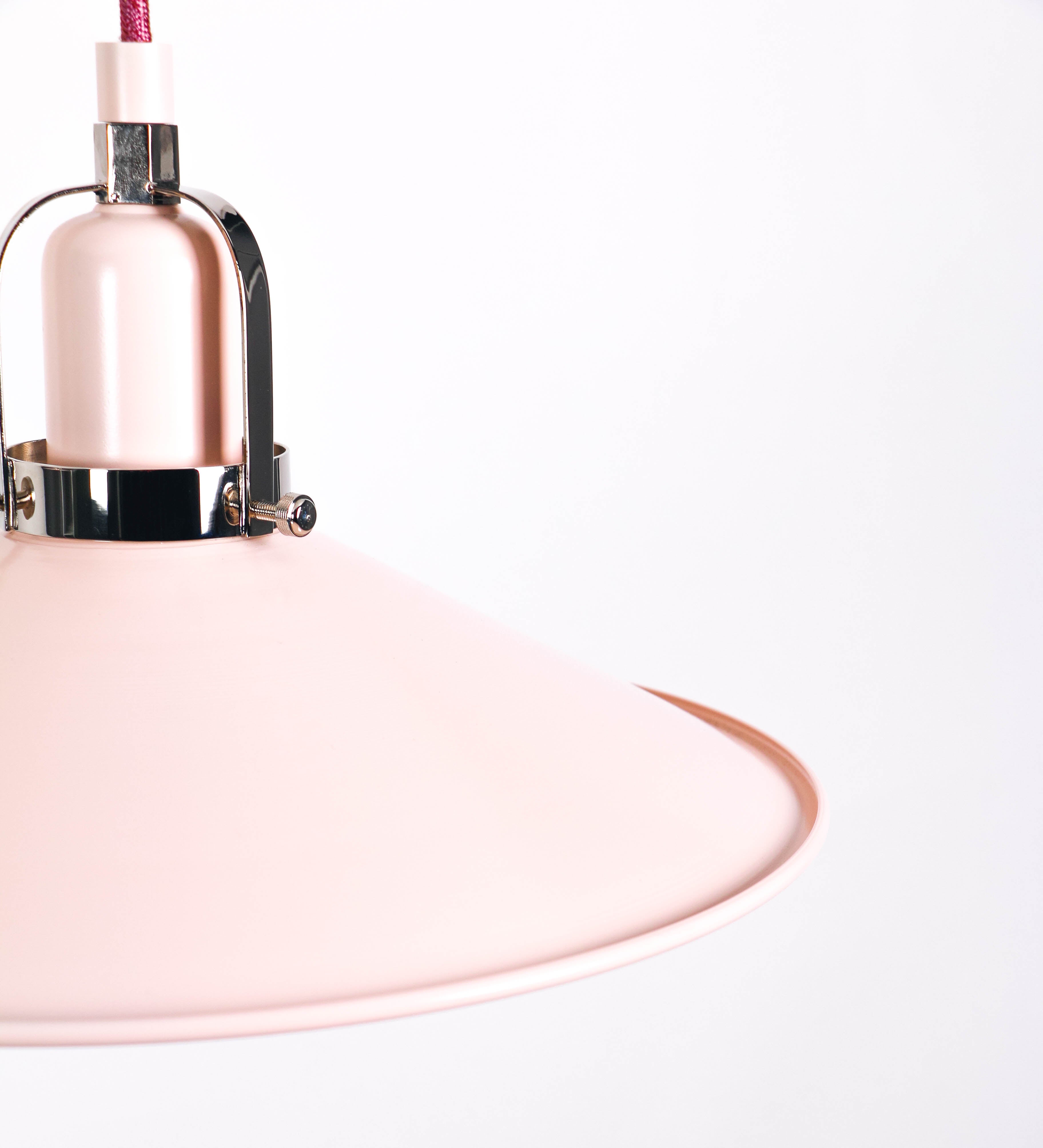 Suspensão de teto dupla composta por uma base circular rosa clara, de onde descem dois cabos revestidos têxtil rosa velho. Cada cabo passa por uma roldana, em níquel polido fixa ao teto, e desce até aos chapéus. Entre a base e as roldanas, cada cabo sustenta uma esfera em níquel polido, que atua como contrapeso para ajustar a altura. Os dois chapéus são rosa claro, de formato cónico invertido e interior branco. No topo de cada chapéu há um suporte em níquel polido que conecta os chapéus aos cabos.