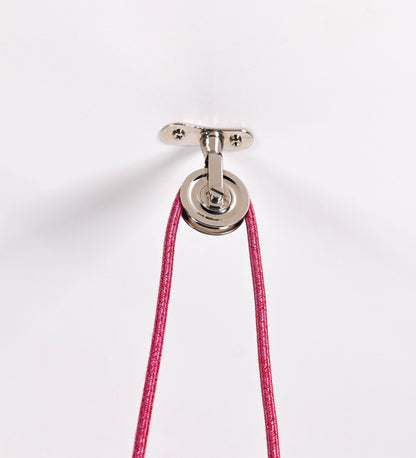Suspensão de teto dupla composta por uma base circular rosa clara, de onde descem dois cabos revestidos têxtil rosa velho. Cada cabo passa por uma roldana, em níquel polido fixa ao teto, e desce até aos chapéus. Entre a base e as roldanas, cada cabo sustenta uma esfera em níquel polido, que atua como contrapeso para ajustar a altura. Os dois chapéus são rosa claro, de formato cónico invertido e interior branco. No topo de cada chapéu há um suporte em níquel polido que conecta os chapéus aos cabos.