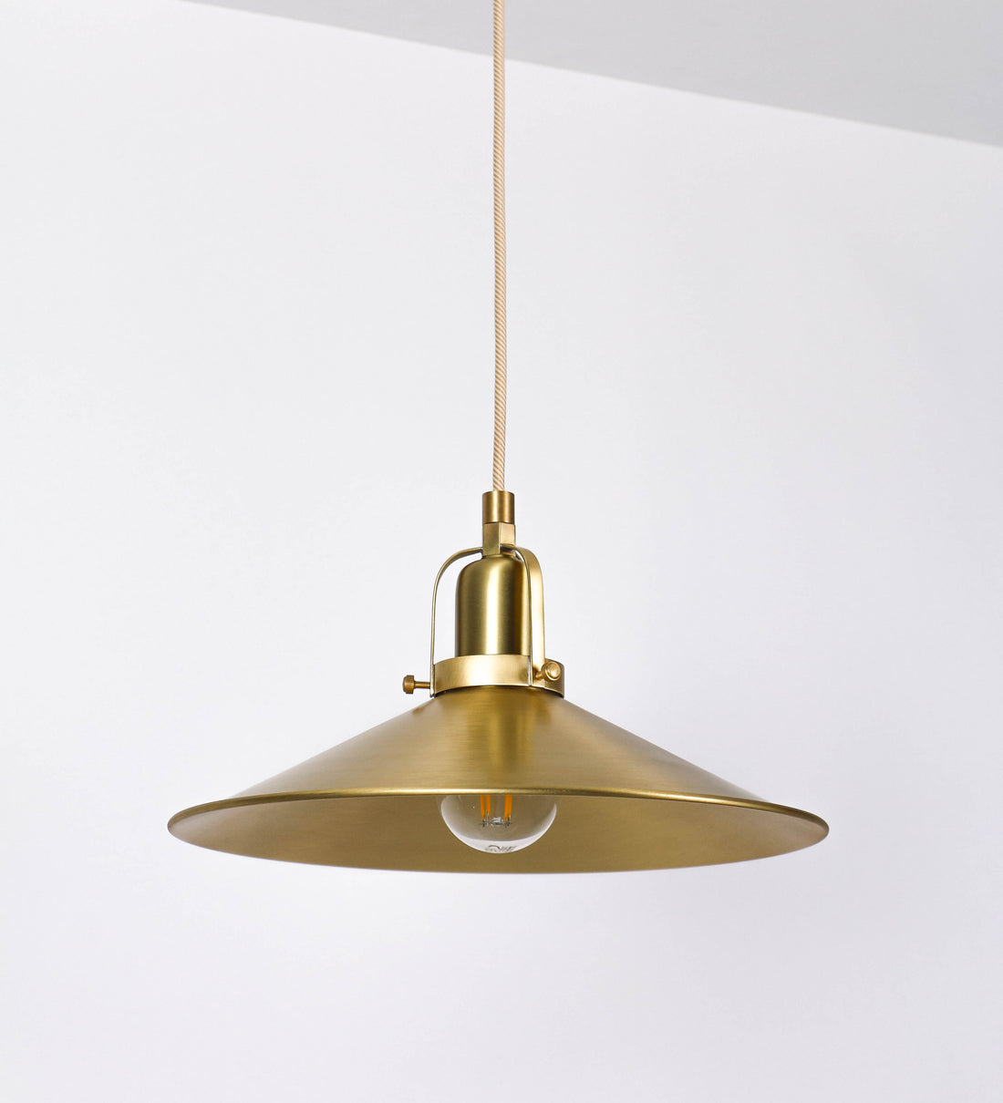 Suspensão de teto que combina um design clássico com um acabamento moderno e sofisticado. A suspensão, toda em latão escovado, é fixa ao teto através de uma base circular de onde desce um cabo revestido têxtil com um padrão trançado com linhas douradas e brancas, que sustenta o chapéu principal. O chapéu tem um formato cónico invertido, com uma borda ligeiramente levantada. No topo do chapéu, há um suporte circular com três pequenos braços que conecta o chapéu ao cabo.