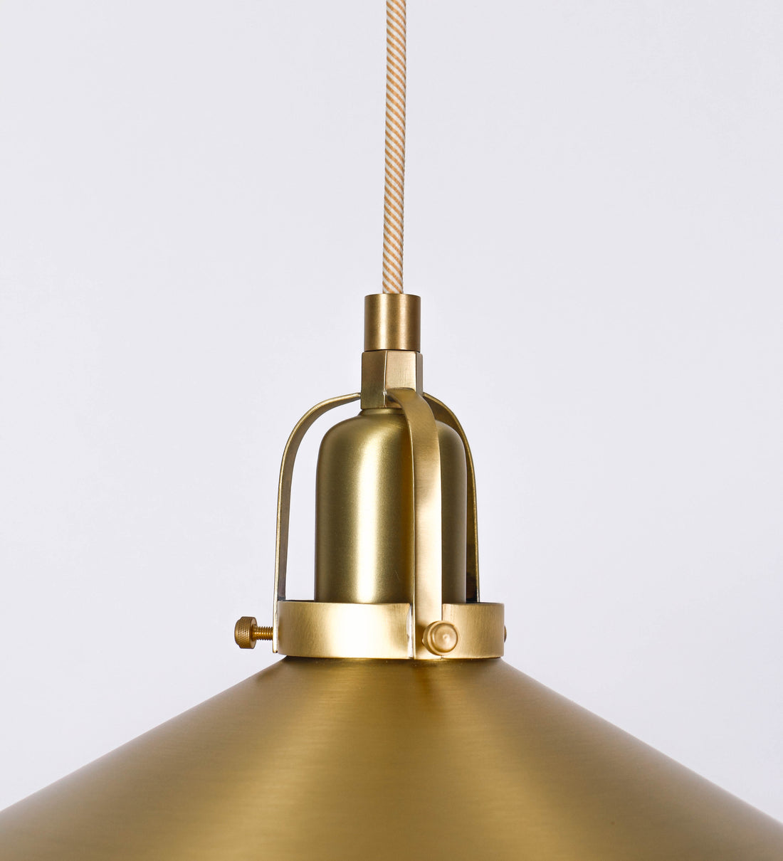 Suspensão de teto que combina um design clássico com um acabamento moderno e sofisticado. A suspensão, toda em latão escovado, é fixa ao teto através de uma base circular de onde desce um cabo revestido têxtil com um padrão trançado com linhas douradas e brancas, que sustenta o chapéu principal. O chapéu tem um formato cónico invertido, com uma borda ligeiramente levantada. No topo do chapéu, há um suporte circular com três pequenos braços que conecta o chapéu ao cabo.