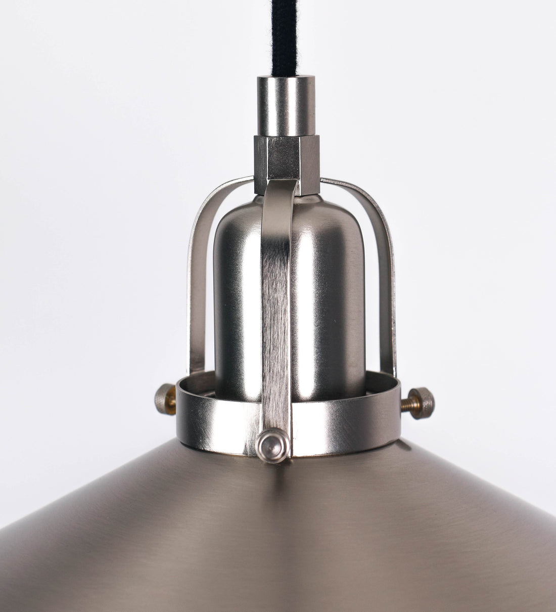 Suspensão de teto que combina um design clássico com um acabamento moderno e de estilo industrial. A suspensão, toda em níquel escovado, é fixa ao teto através de uma base circular de onde desce um cabo revestido têxtil preto, que sustenta o chapéu principal. O chapéu tem um formato cónico invertido, com uma borda ligeiramente levantada. No topo do chapéu, há um suporte circular com três pequenos braços que conecta o chapéu ao cabo.