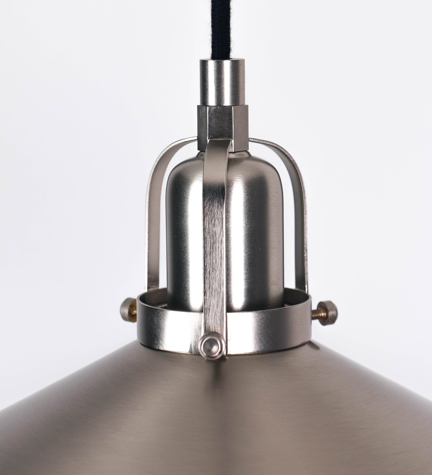 Suspensão de teto que combina um design clássico com um acabamento moderno e de estilo industrial. A suspensão, toda em níquel escovado, é fixa ao teto através de uma base circular de onde desce um cabo revestido têxtil preto, que sustenta o chapéu principal. O chapéu tem um formato cónico invertido, com uma borda ligeiramente levantada. No topo do chapéu, há um suporte circular com três pequenos braços que conecta o chapéu ao cabo.