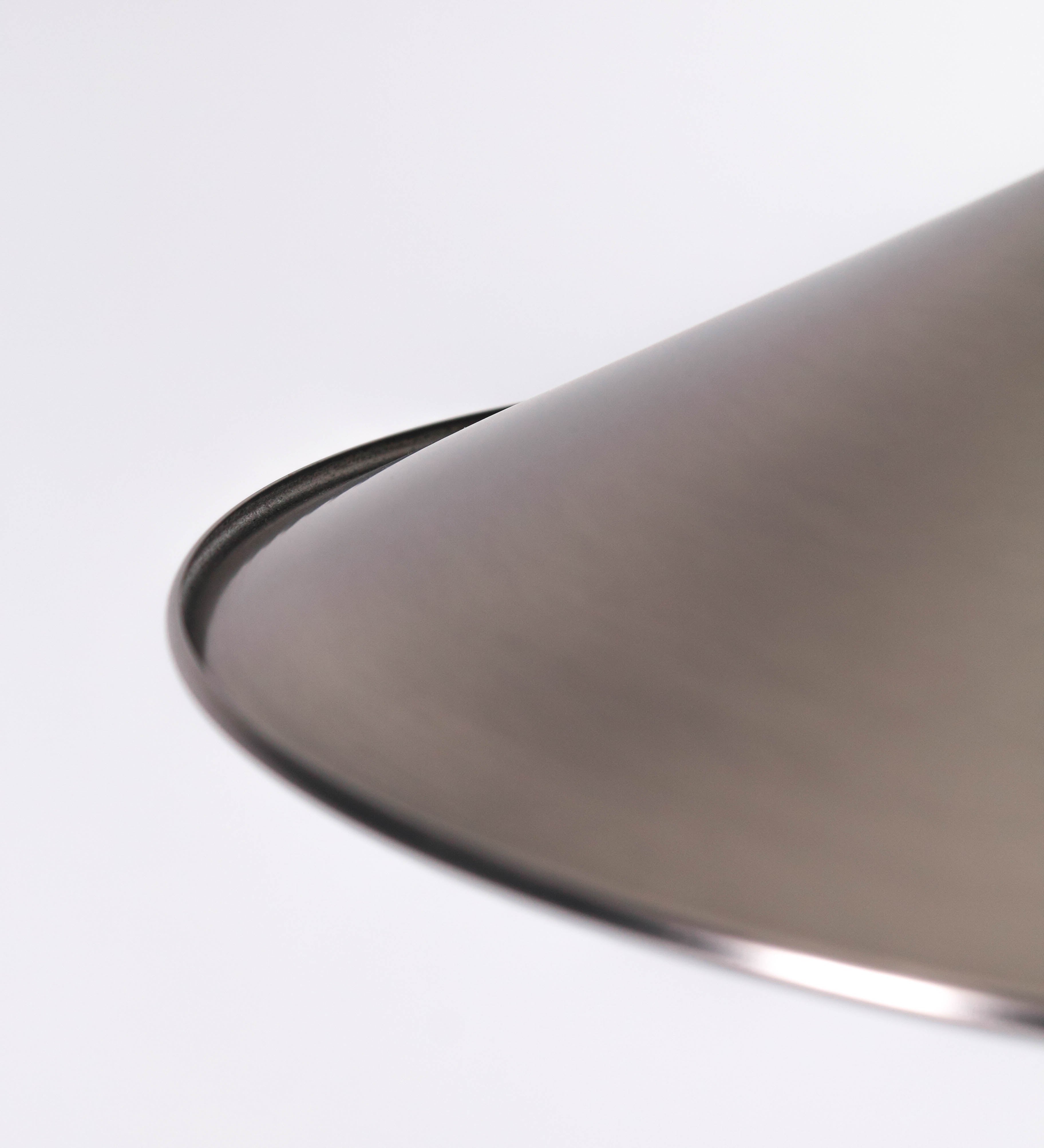 Suspensão de teto que combina um design clássico com um acabamento moderno e de estilo industrial. A suspensão, toda em níquel escovado, é fixa ao teto através de uma base circular de onde desce um cabo revestido têxtil preto, que sustenta o chapéu principal. O chapéu tem um formato cónico invertido, com uma borda ligeiramente levantada. No topo do chapéu, há um suporte circular com três pequenos braços que conecta o chapéu ao cabo.