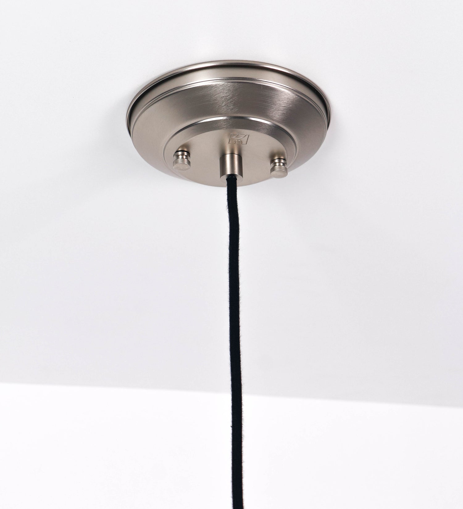 Suspensão de teto que combina um design clássico com um acabamento moderno e de estilo industrial. A suspensão, toda em níquel escovado, é fixa ao teto através de uma base circular de onde desce um cabo revestido têxtil preto, que sustenta o chapéu principal. O chapéu tem um formato cónico invertido, com uma borda ligeiramente levantada. No topo do chapéu, há um suporte circular com três pequenos braços que conecta o chapéu ao cabo.