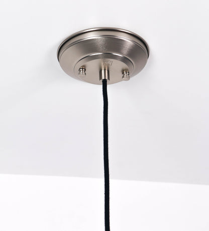 Suspensão de teto que combina um design clássico com um acabamento moderno e de estilo industrial. A suspensão, toda em níquel escovado, é fixa ao teto através de uma base circular de onde desce um cabo revestido têxtil preto, que sustenta o chapéu principal. O chapéu tem um formato cónico invertido, com uma borda ligeiramente levantada. No topo do chapéu, há um suporte circular com três pequenos braços que conecta o chapéu ao cabo.