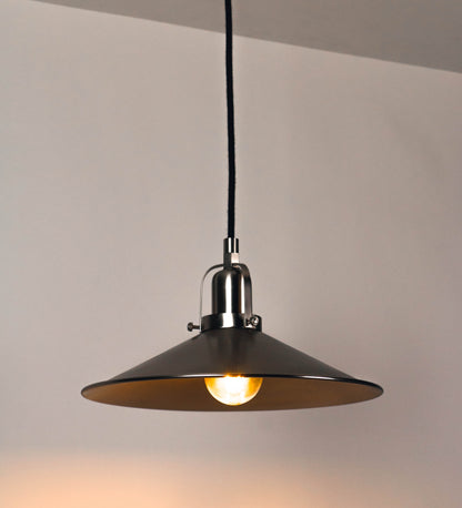 Suspensão de teto que combina um design clássico com um acabamento moderno e de estilo industrial. A suspensão, toda em níquel escovado, é fixa ao teto através de uma base circular de onde desce um cabo revestido têxtil preto, que sustenta o chapéu principal. O chapéu tem um formato cónico invertido, com uma borda ligeiramente levantada. No topo do chapéu, há um suporte circular com três pequenos braços que conecta o chapéu ao cabo.