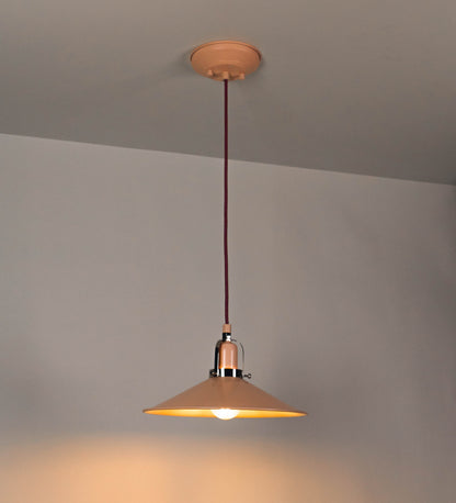 Suspensão de teto que combina um design clássico com cores modernas. A suspensão é fixa ao teto através de uma base circular rosa clara, de onde desce um cabo revestido têxtil rosa velho, que sustenta o chapéu principal. O chapéu, rosa claro, tem um formato cónico invertido, com uma borda ligeiramente levantada. O interior do chapéu é branco. No topo do chapéu, há um suporte circular em níquel polido, com três pequenos braços que conecta o chapéu ao cabo.