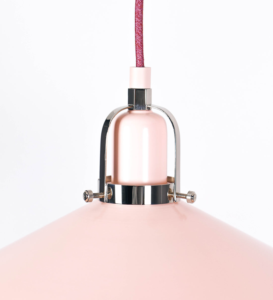 Suspensão de teto que combina um design clássico com cores modernas. A suspensão é fixa ao teto através de uma base circular rosa clara, de onde desce um cabo revestido têxtil rosa velho, que sustenta o chapéu principal. O chapéu, rosa claro, tem um formato cónico invertido, com uma borda ligeiramente levantada. O interior do chapéu é branco. No topo do chapéu, há um suporte circular em níquel polido, com três pequenos braços que conecta o chapéu ao cabo.