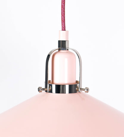 Suspensão de teto que combina um design clássico com cores modernas. A suspensão é fixa ao teto através de uma base circular rosa clara, de onde desce um cabo revestido têxtil rosa velho, que sustenta o chapéu principal. O chapéu, rosa claro, tem um formato cónico invertido, com uma borda ligeiramente levantada. O interior do chapéu é branco. No topo do chapéu, há um suporte circular em níquel polido, com três pequenos braços que conecta o chapéu ao cabo.