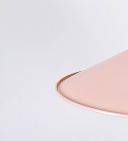 Suspensão de teto que combina um design clássico com cores modernas. A suspensão é fixa ao teto através de uma base circular rosa clara, de onde desce um cabo revestido têxtil rosa velho, que sustenta o chapéu principal. O chapéu, rosa claro, tem um formato cónico invertido, com uma borda ligeiramente levantada. O interior do chapéu é branco. No topo do chapéu, há um suporte circular em níquel polido, com três pequenos braços que conecta o chapéu ao cabo.