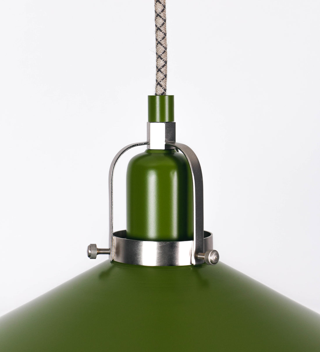 Suspensão de teto que combina um design clássico e cores modernas. A suspensão é fixa ao teto através de uma base circular verde couve-de-bruxelas, de onde desce um cabo revestido têxtil com um padrão de linhas castanhas e beges entrelaçadas, que sustenta o chapéu principal. O chapéu, verde, tem um formato cónico invertido, com uma borda ligeiramente levantada. O interior do chapéu é branco. No topo do chapéu, há um suporte circular em níquel escovado, com três pequenos braços que conecta o chapéu ao cabo.