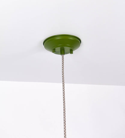 Suspensão de teto que combina um design clássico e cores modernas. A suspensão é fixa ao teto através de uma base circular verde couve-de-bruxelas, de onde desce um cabo revestido têxtil com um padrão de linhas castanhas e beges entrelaçadas, que sustenta o chapéu principal. O chapéu, verde, tem um formato cónico invertido, com uma borda ligeiramente levantada. O interior do chapéu é branco. No topo do chapéu, há um suporte circular em níquel escovado, com três pequenos braços que conecta o chapéu ao cabo.